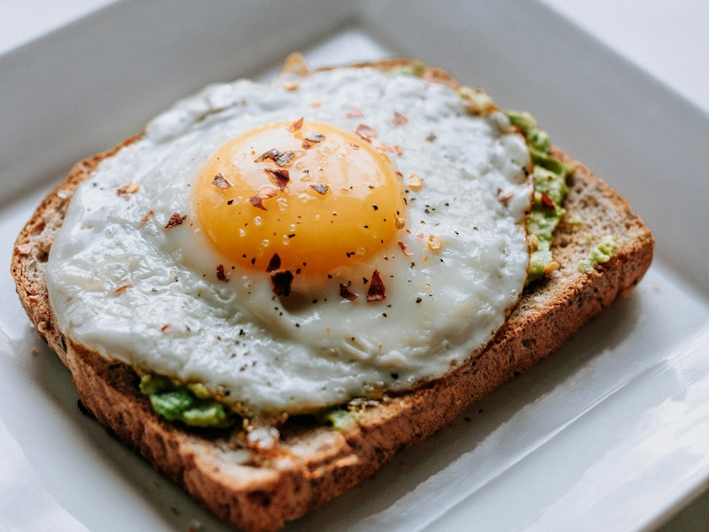 Close-up of a fried egg on avocado toast on a white plate